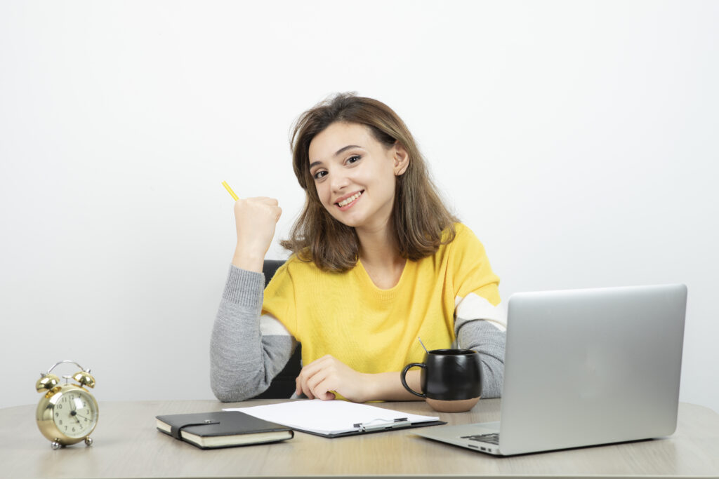 Photo of female office worker sitting at the desk with laptop and clipboard