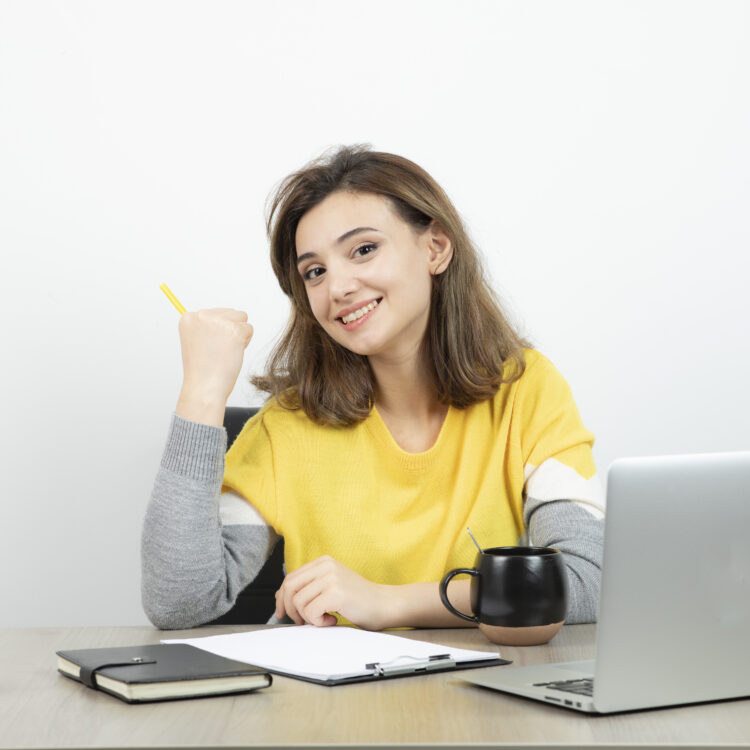 Photo of female office worker sitting at the desk with laptop and clipboard